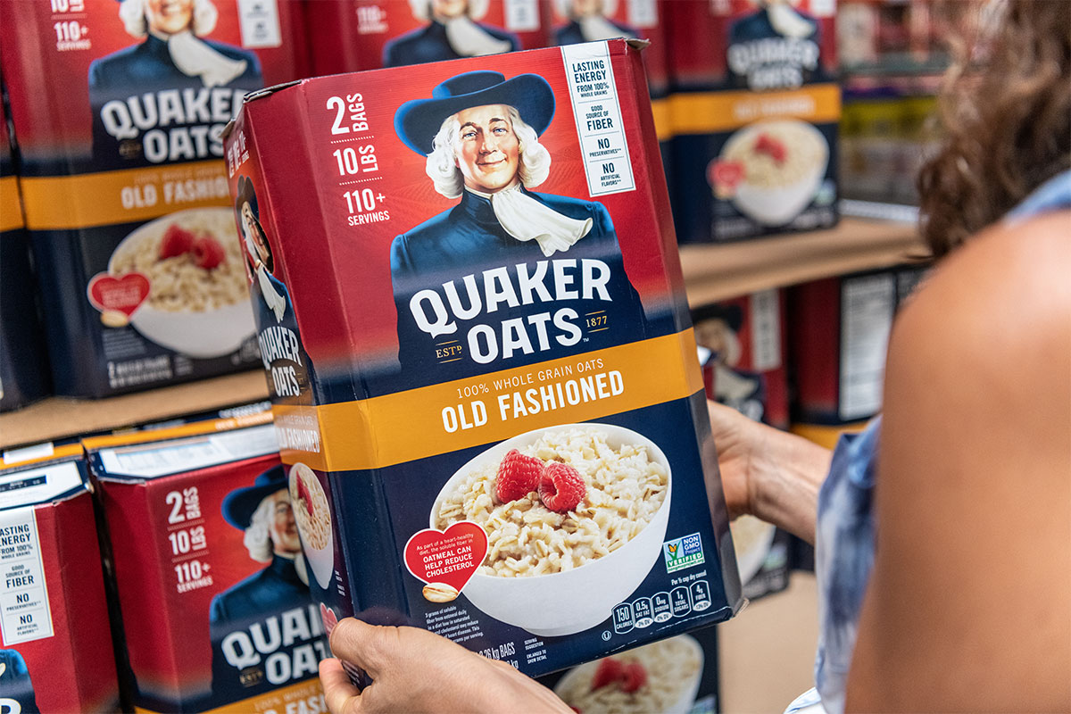 A woman holds a box of Quaker oats inside a grocery store. 
