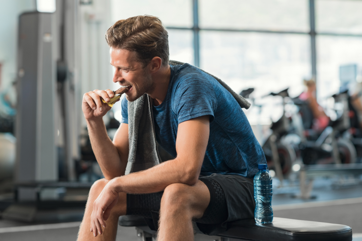 Athletic man eating protein bar at the gym