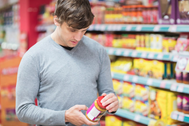 Man looking at nutrient content claim on peanut butter in supermarket