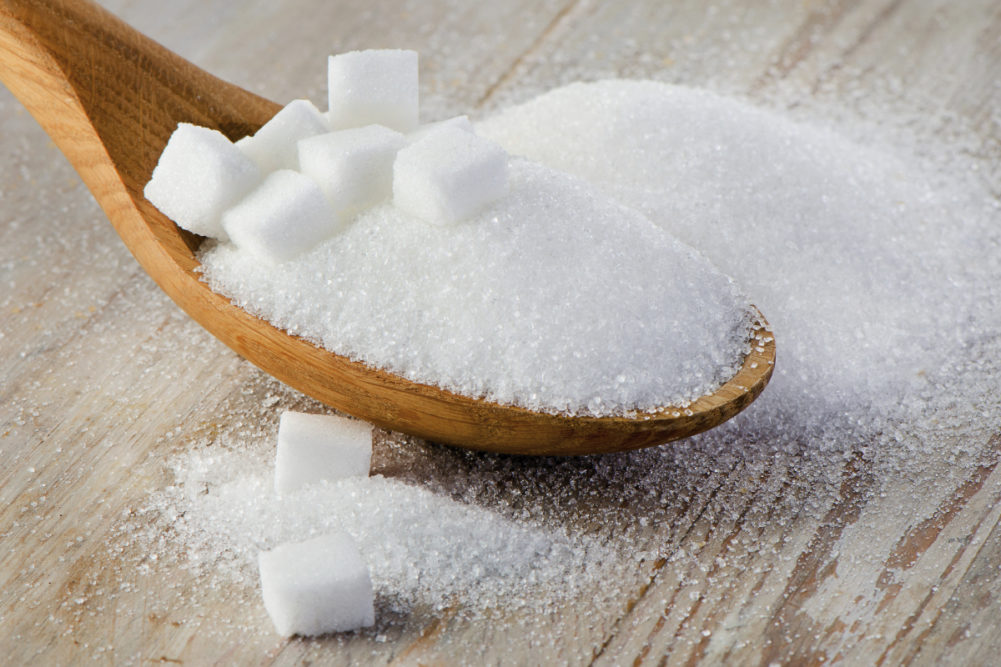 Wooden spoon full of sugar and sugar cubes