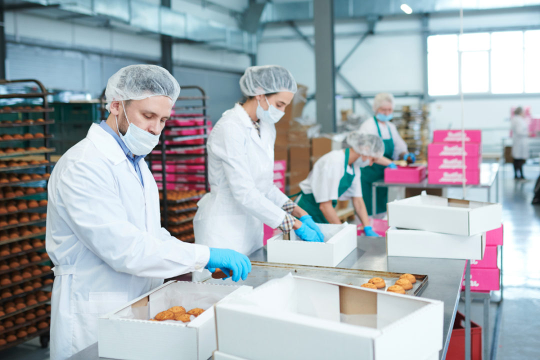 Bakery workers wearing masks and gloves packing pastries into boxes