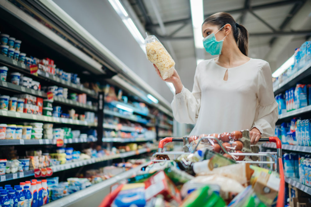 Woman wearing face mask grocery shopping for packaged foods