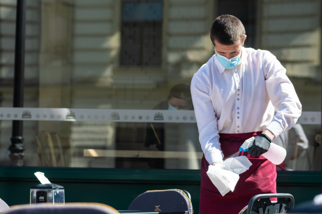 waiter with mask disinfects tables at a restaurant