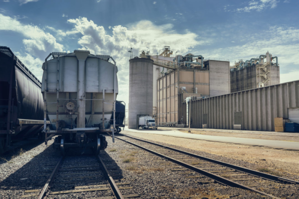  rail road track with cargo containers, silo and large facility in distance