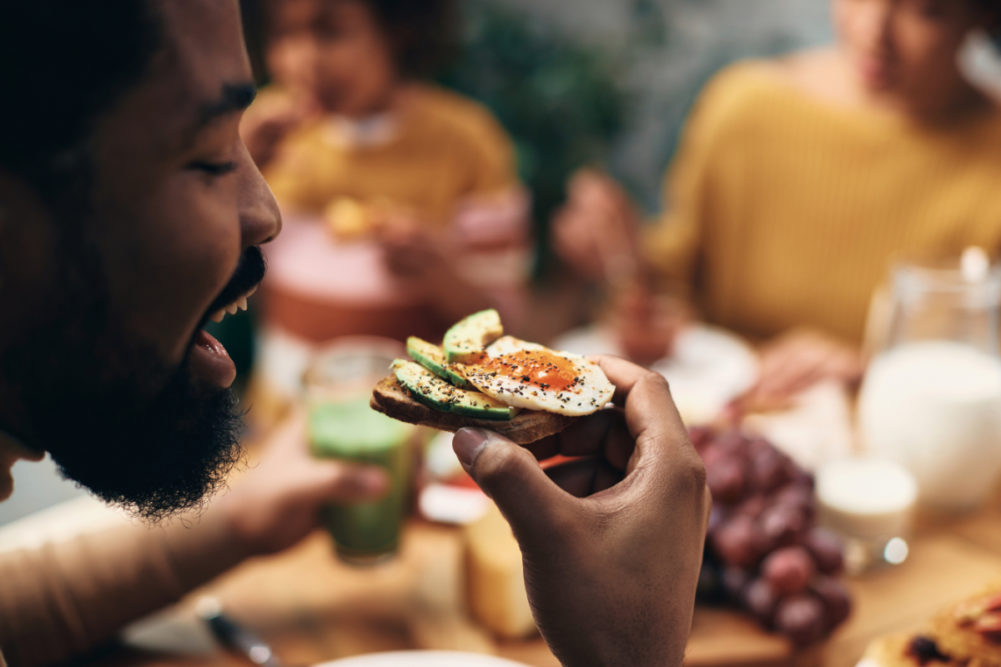 Black man eating avocado toast with his family at home.