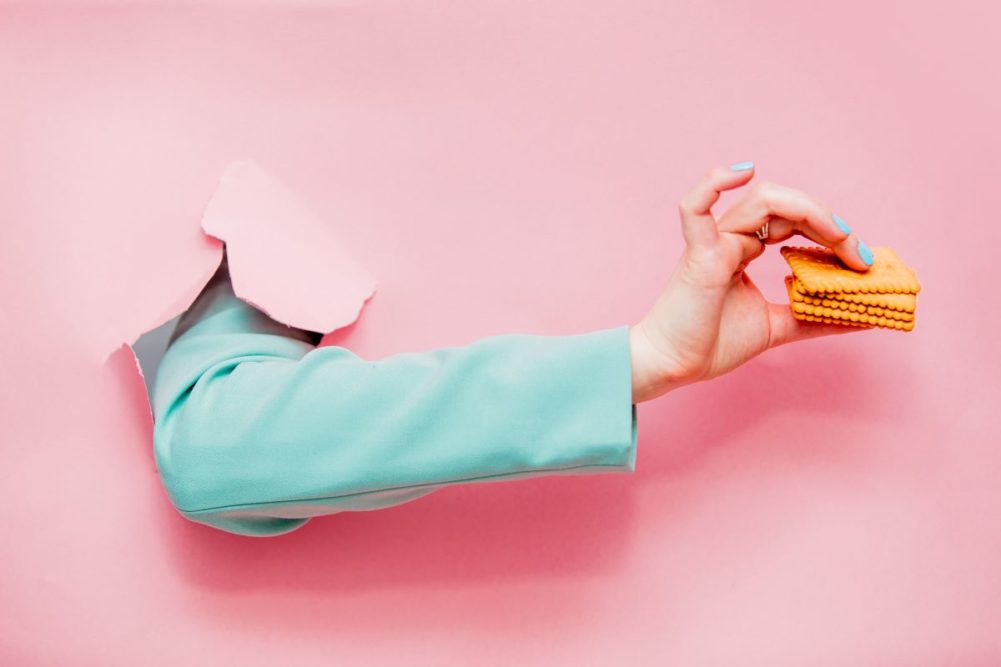 Arm holding cookies, pink paper, blue jacket sleeve