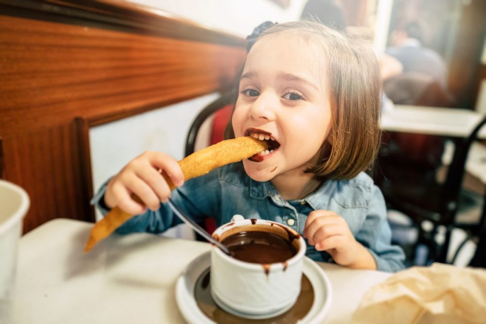 Child eating churro dipped in chocolate