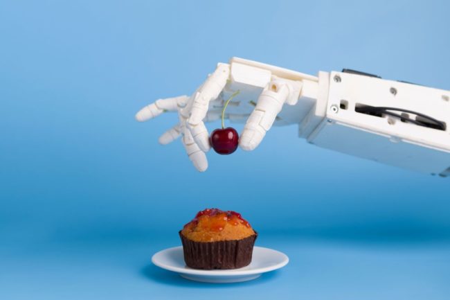 Robot hand placing cherry on a cupcake