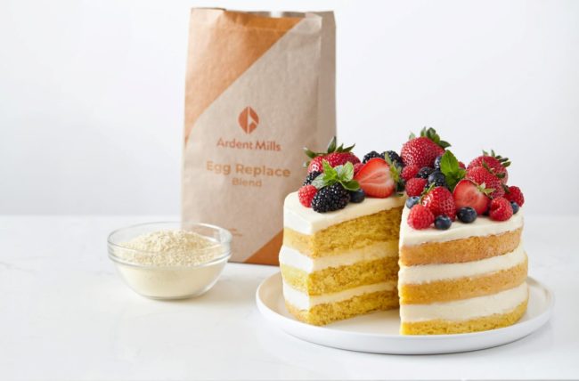 Vanilla cake with berries in front of the Ardent Mills Egg Replacement Product