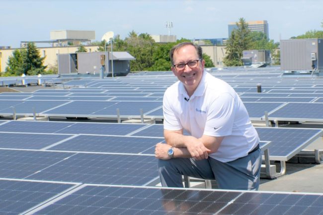 Joe Ennen, chief executive officer of SunOpta, kneels next to the company’s newly installed solar panels. 