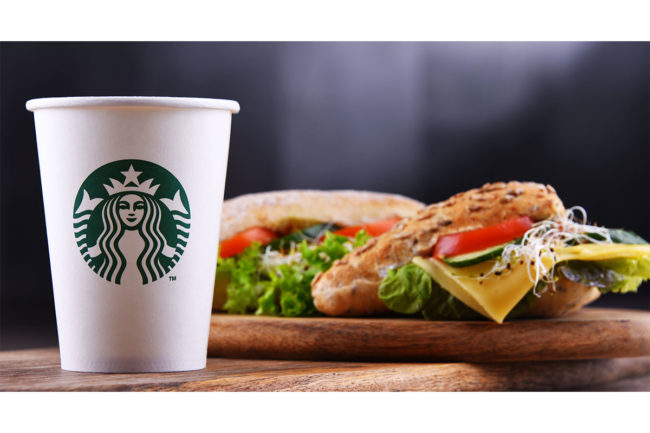 A cup of Starbucks coffee next to a breakfast sandwich. 