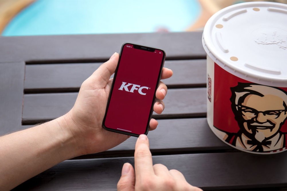 KFC app pulled up on phone next to bucket of KFC chicken. 