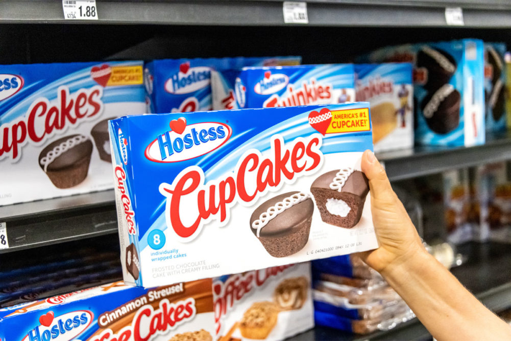 Hand holds Hostess cupcakes in grocery store. 