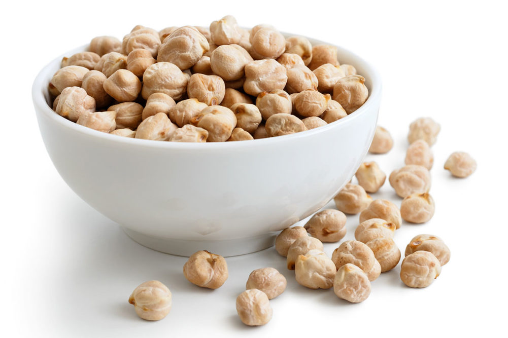 Bowl of chickpeas in front of white background. 