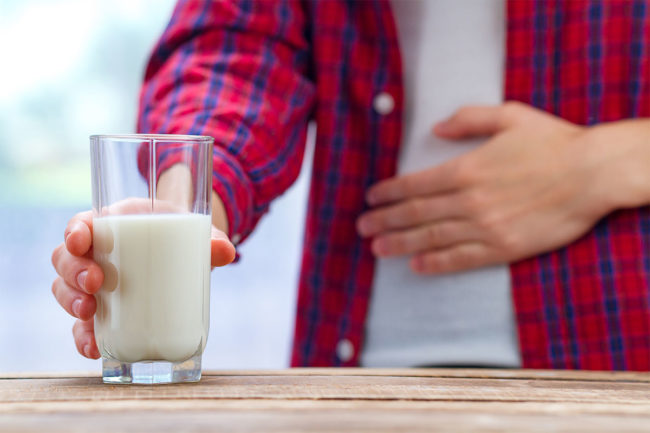 Man holds stomach after drinking glass of milk, indicating lactose intolerance. 