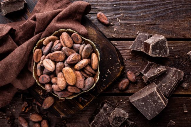 A bowl of cocoa beans and chocolate on a wooden table. 