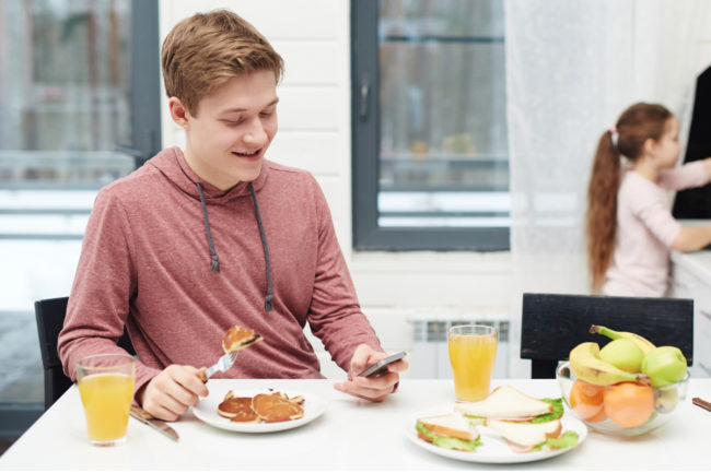 Gen Z boy eating and looking at phone